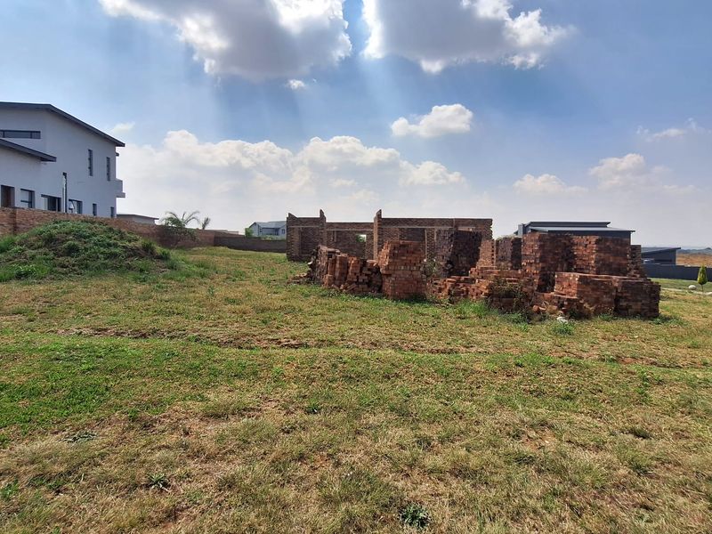 A vacant residential plot featuring ongoing construction with exposed brickwork and boundary walls under a clear sky.