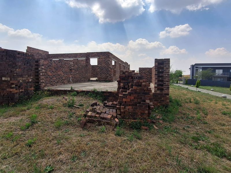 An unfinished residential construction site showing exposed brick walls and a concrete foundation slab in a developing estate.