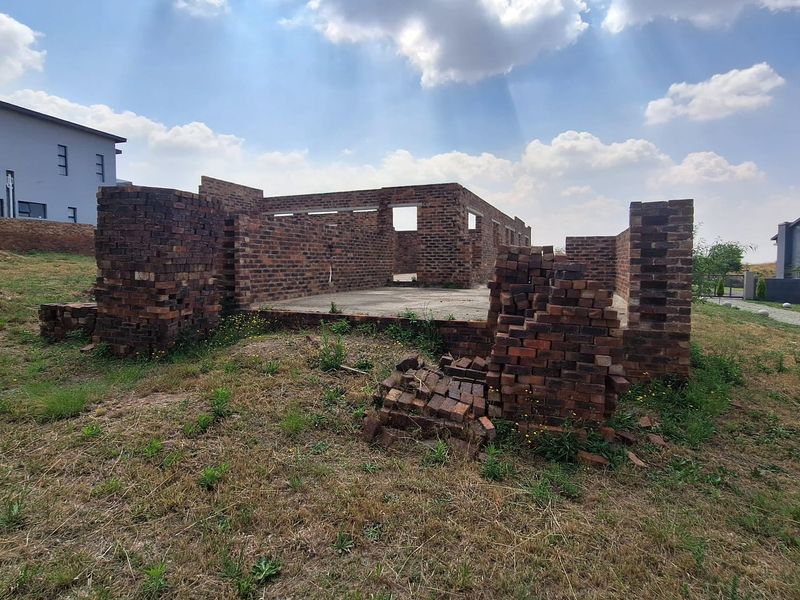 An incomplete residential construction site showing exposed brick walls and a concrete foundation slab on a vacant plot.