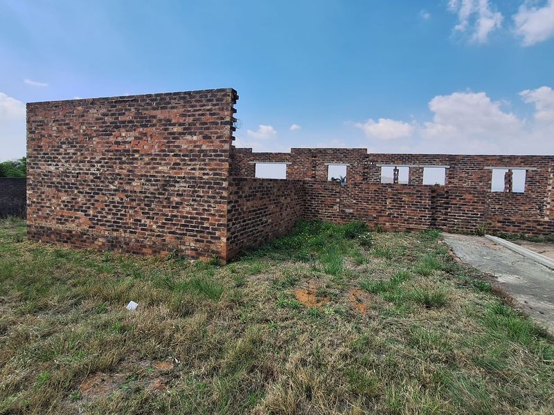 An unfinished brick structure showing the exterior shell of a property under construction, set on a grassy plot.