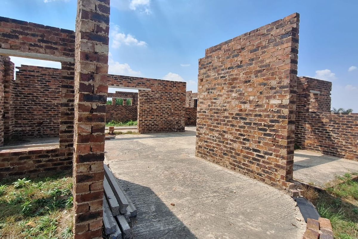 An unfinished residential construction site showing exposed brick walls and a concrete slab foundation under a clear sky.