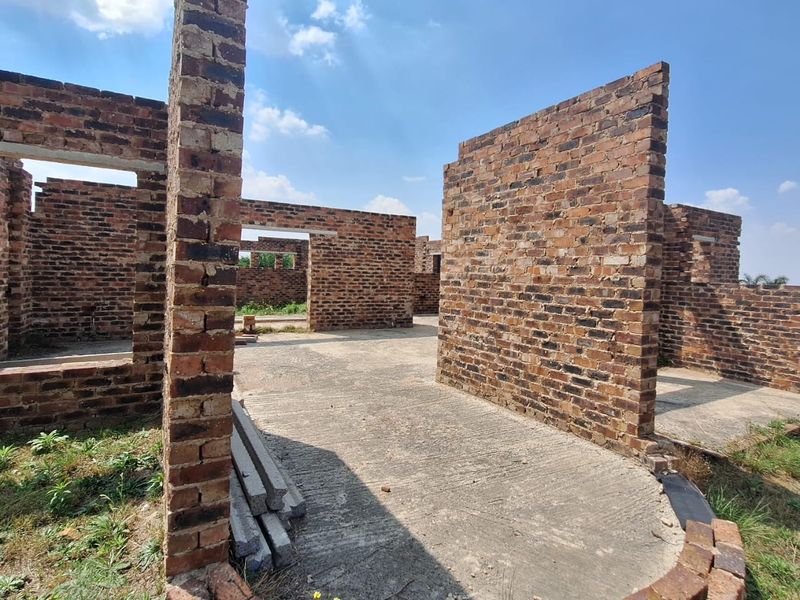 An unfinished residential construction site showing exposed brick walls and a concrete slab foundation under a clear sky.