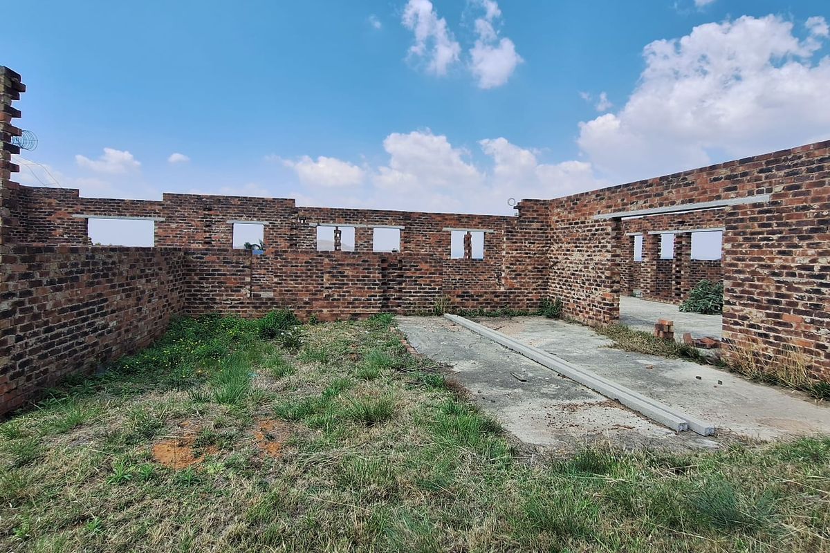 An unfinished construction site featuring exposed brick walls and a concrete slab foundation, currently in a shell state without roofing or fixtures.