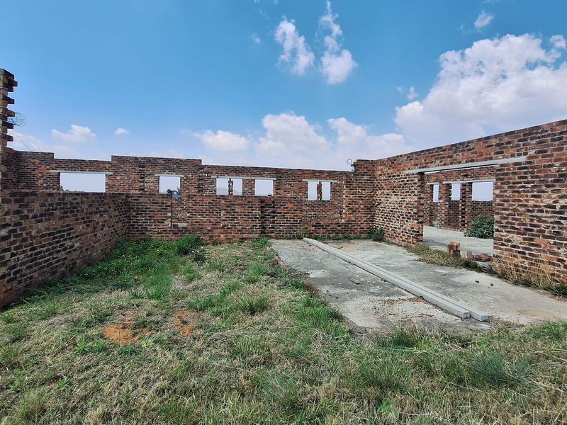 An unfinished construction site featuring exposed brick walls and a concrete slab foundation, currently in a shell state without roofing or fixtures.