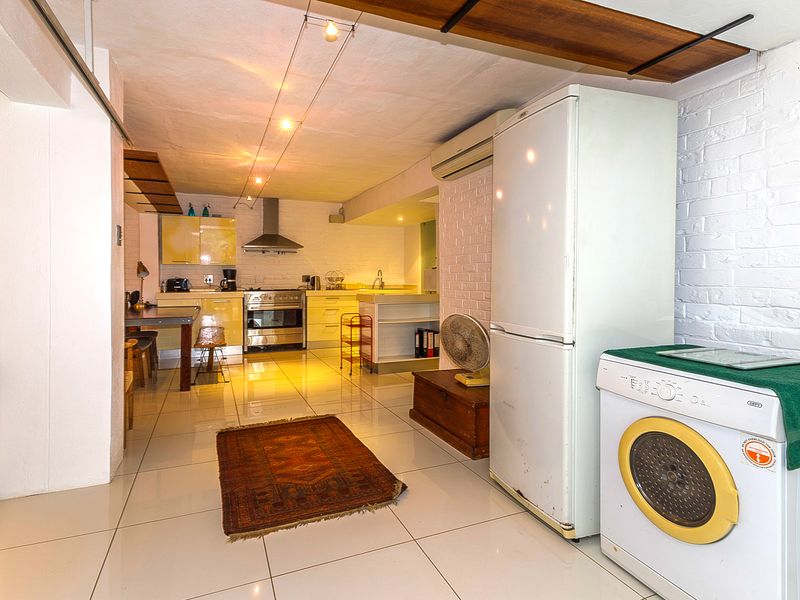 Open-plan kitchen and utility area featuring tiled flooring, exposed brick walls, stainless steel stove, and built-in cabinetry with integrated laundry space.