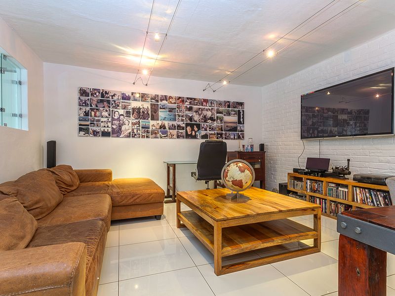 A well-lit living room featuring white painted brick walls, modern tiled flooring, and integrated track lighting, creating a bright and functional living space.