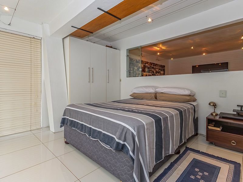 A well-maintained bedroom featuring tiled flooring, built-in wardrobes, track lighting, and a unique glass partition wall providing an open feel.