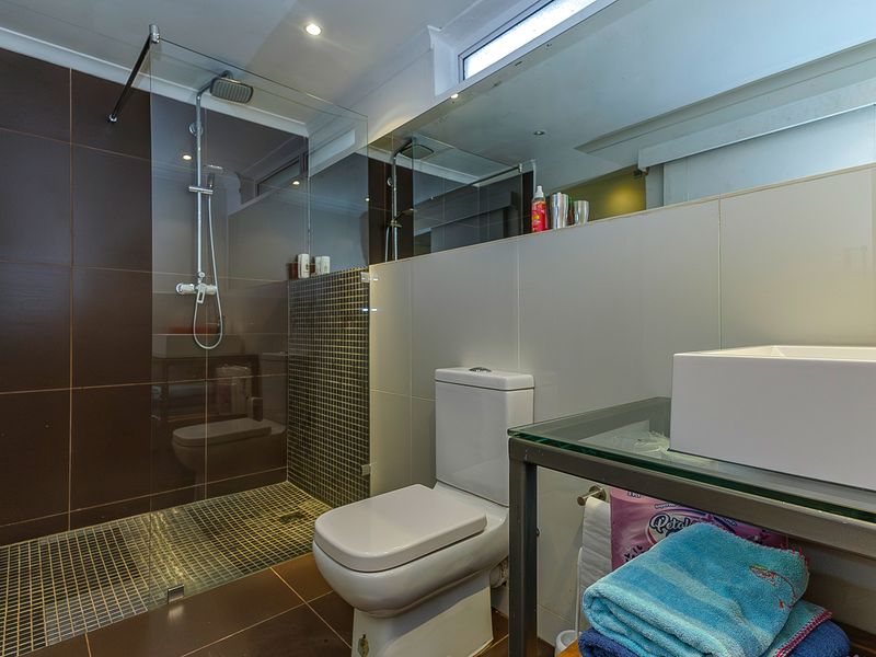 Modern bathroom featuring a walk-in shower with mosaic tiling, a glass vanity with a vessel sink, and a large wall mirror.