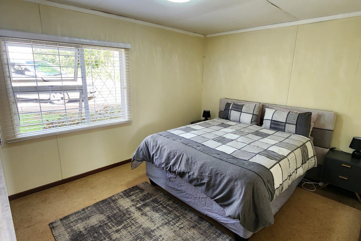 A bedroom featuring carpet flooring, wall paneling, and a window with venetian blinds, offering a functional space with potential for cosmetic updates.