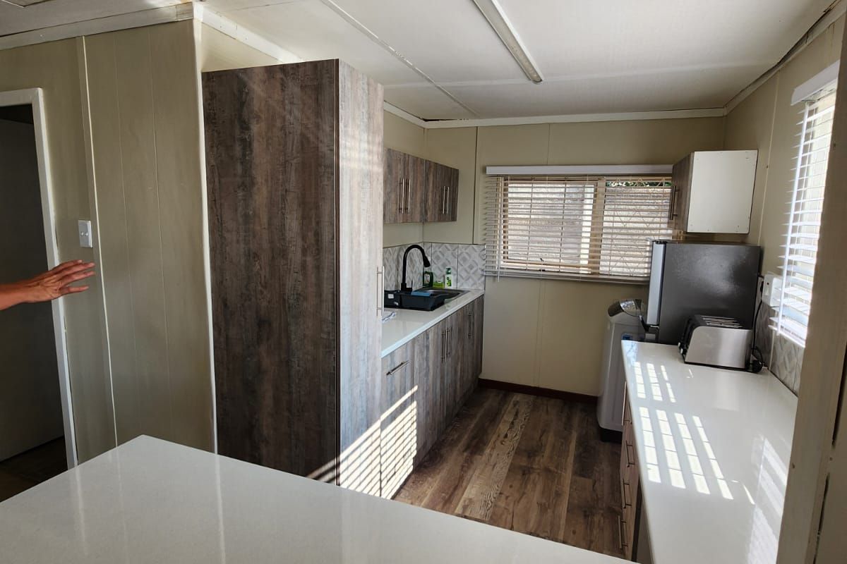 Compact kitchen featuring modern wood-look cabinetry, stone-style countertops, and vinyl flooring, offering a functional layout with natural light from window blinds.