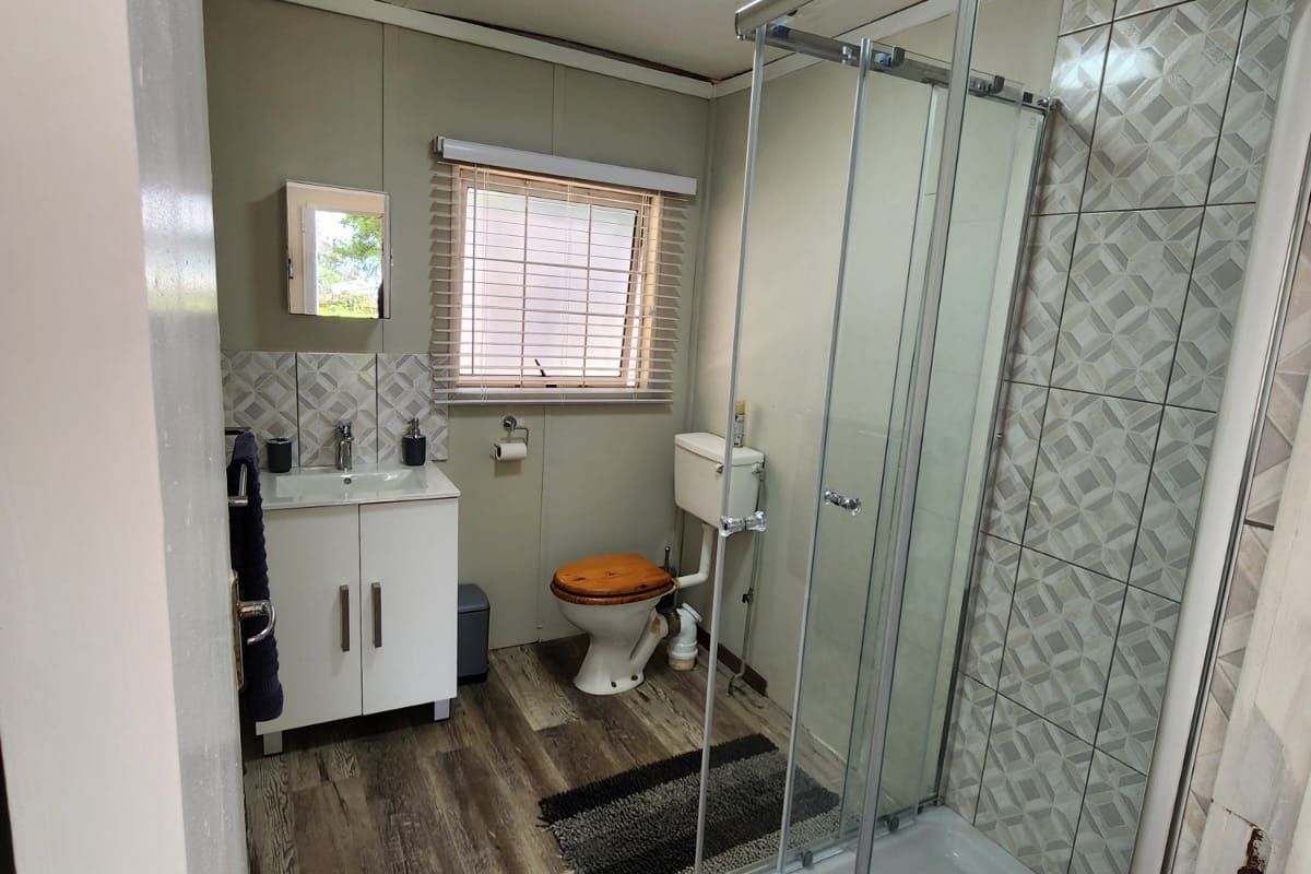 A functional bathroom featuring a glass shower enclosure, vanity basin, and toilet, finished with wood-look laminate flooring and decorative wall tiling.