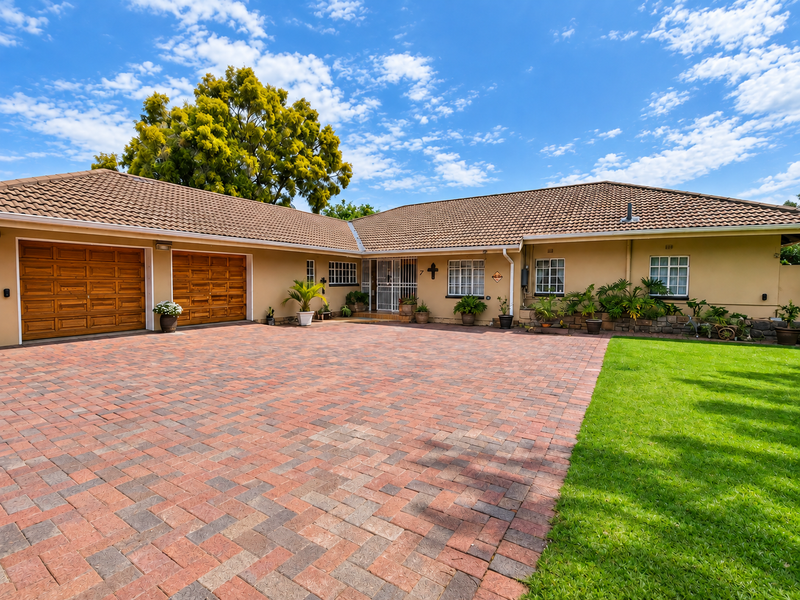 Front elevation of a well-maintained house featuring a paved driveway, double garage, and landscaped garden area.