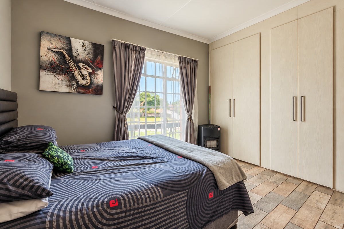 A well-maintained bedroom featuring built-in cupboards, tiled flooring, and a window with security bars, offering a clean and functional living space.