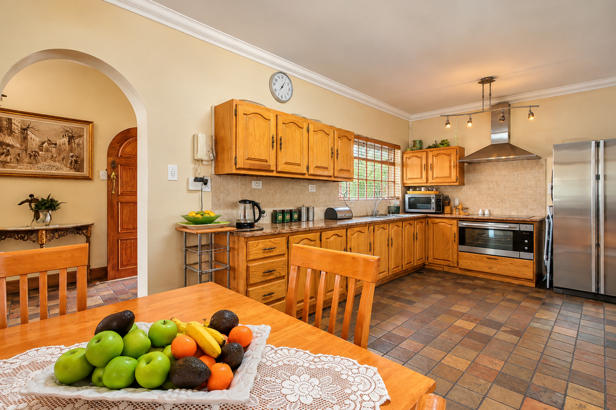 A traditional kitchen featuring wooden cabinetry, granite countertops, and tiled flooring, connected to an adjacent space via a classic archway.