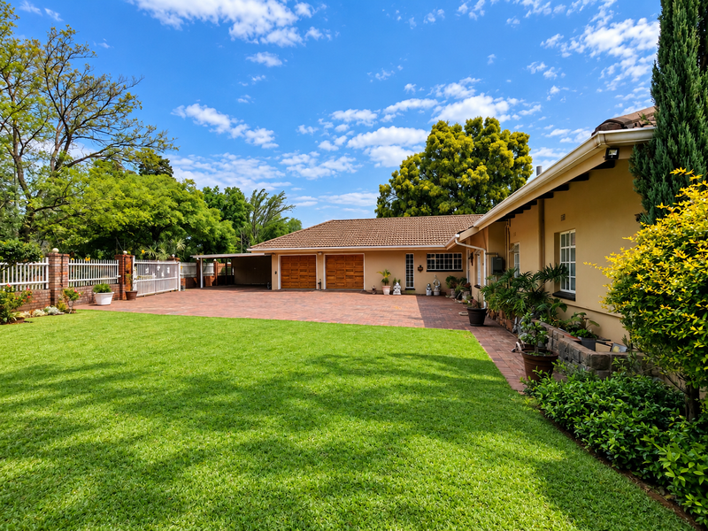 A well-maintained rear exterior view featuring a spacious paved driveway, double garage, and a neatly landscaped lawn with established garden borders.