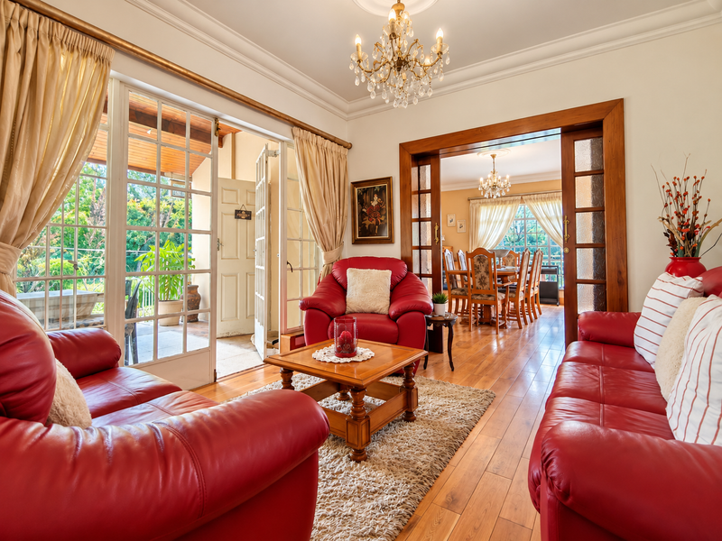 A well-maintained living room featuring hardwood flooring, elegant crown molding, and large french doors that open onto a covered patio area.