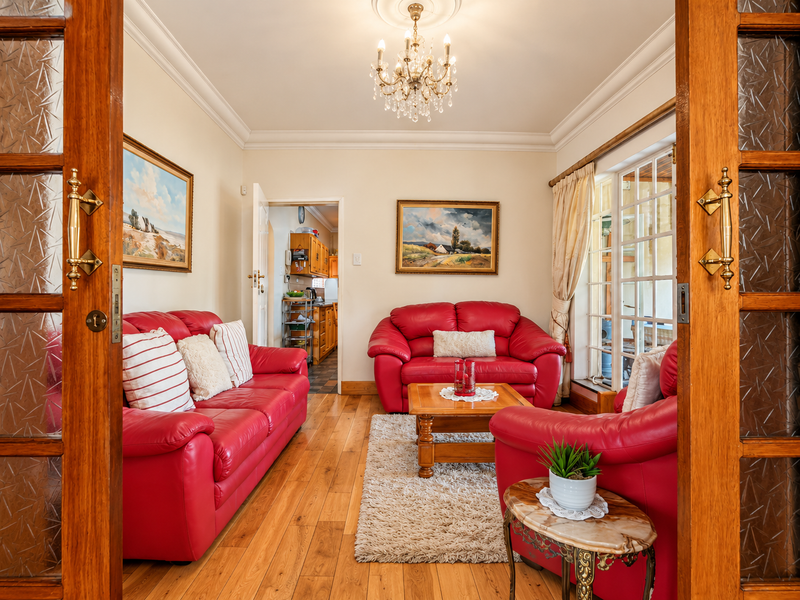 A well-maintained living room featuring hardwood flooring, crown molding, and a crystal chandelier, with direct access to an adjacent kitchen area.