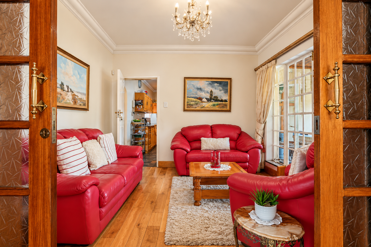 A well-maintained living room featuring hardwood flooring, crown molding, and a crystal chandelier, with direct access to an adjacent kitchen area.