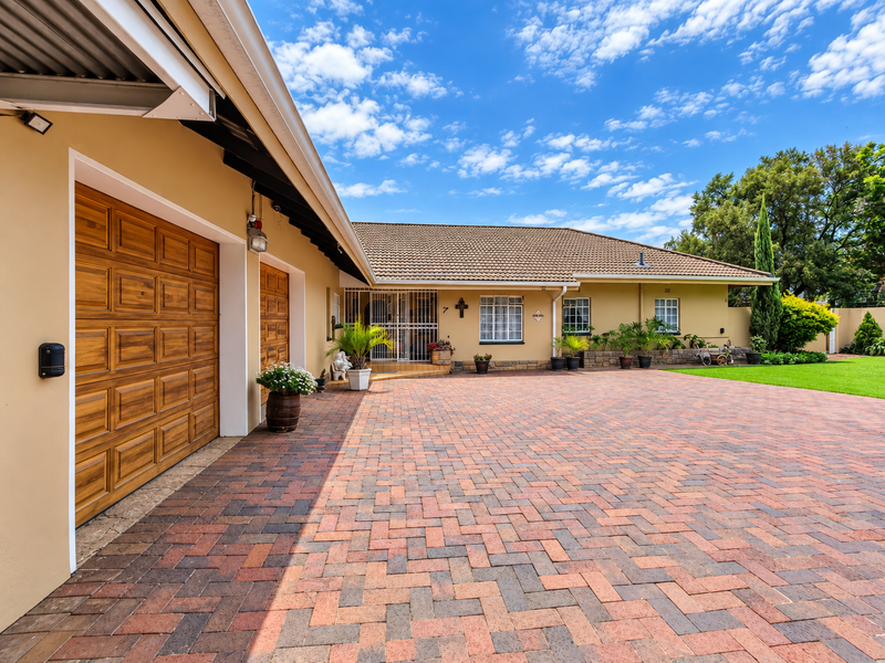 Well-maintained front exterior featuring a spacious paved driveway, double garage, and a neat brick facade with secure entrance.