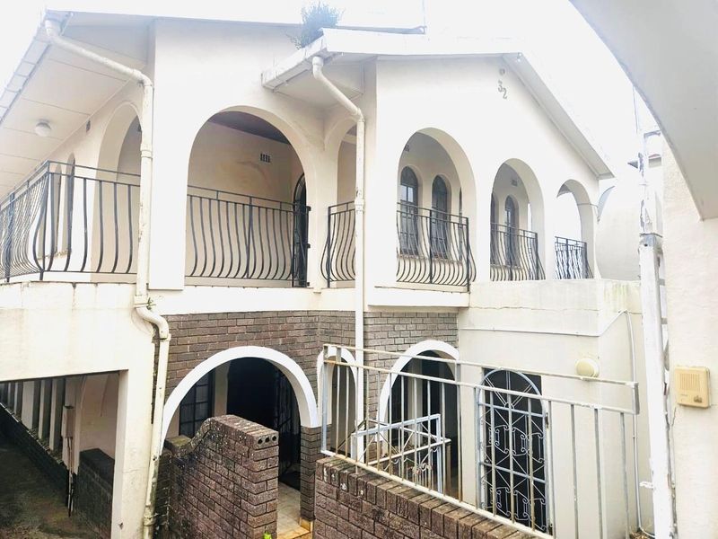 Two-story residential facade featuring arched balconies with wrought iron railings and a combination of brick and painted wall finishes.