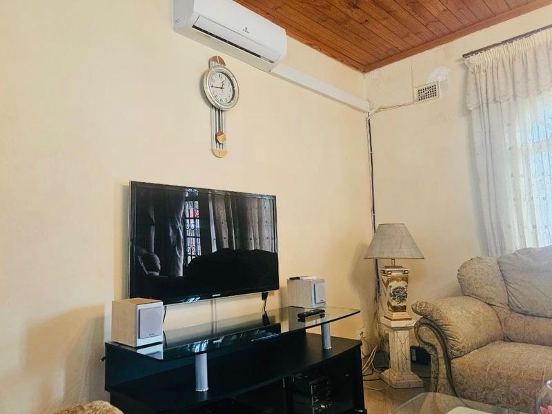Living room featuring a timber ceiling and wall-mounted air conditioning unit, showing signs of wear including visible wall cracks and exposed wiring.