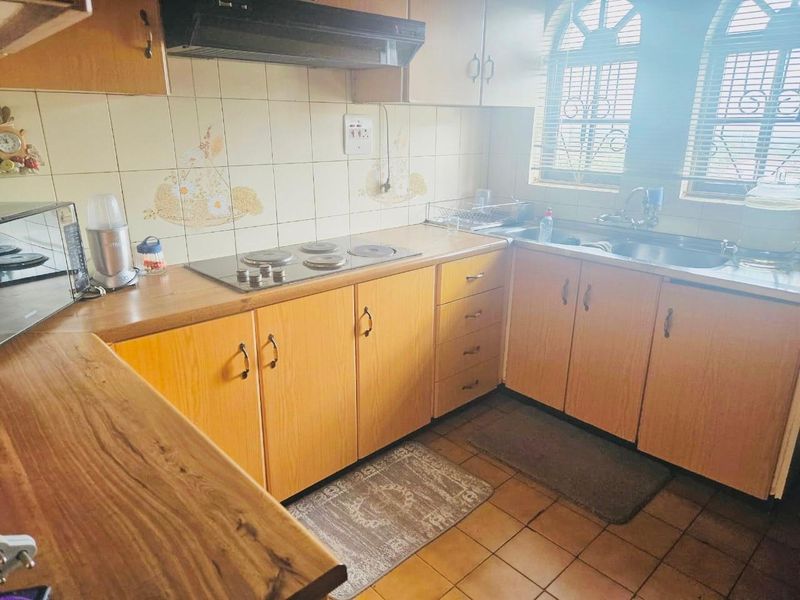 A functional kitchen featuring laminate cabinetry, an electric hob with extractor fan, tiled backsplash, and a stainless steel sink.
