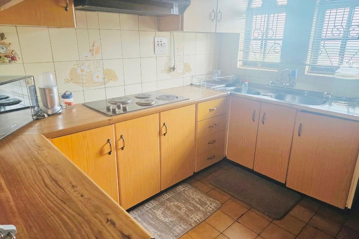 A functional kitchen featuring laminate cabinetry, an electric hob with extractor fan, tiled backsplash, and a stainless steel sink.
