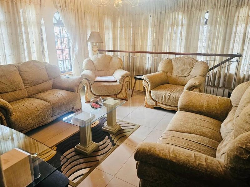 A spacious living room featuring tiled flooring, arched windows with curtains, and a metal balustrade overlooking a lower level.