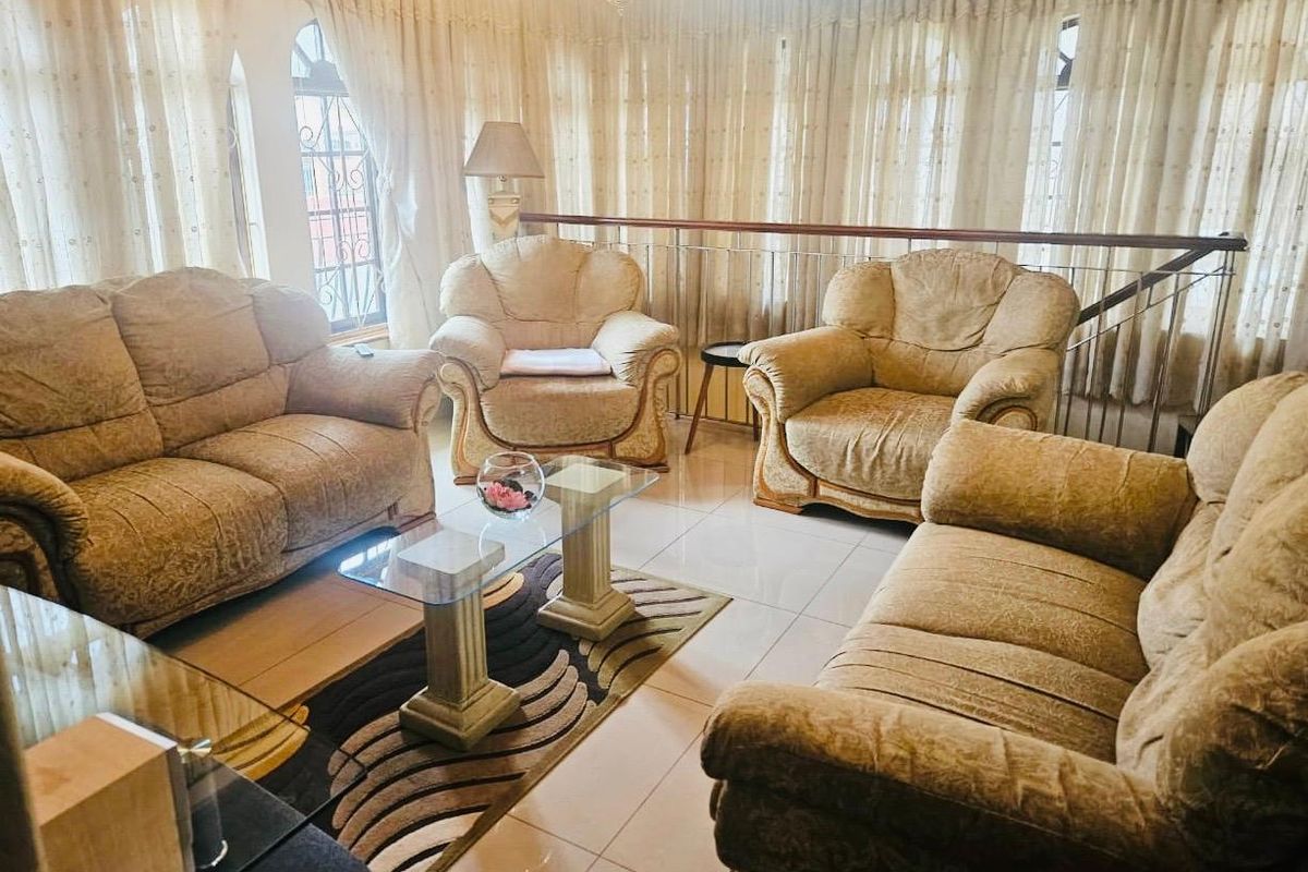 A spacious living room featuring tiled flooring, arched windows with curtains, and a metal balustrade overlooking a lower level.