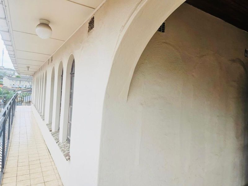 A covered balcony featuring tiled flooring, arched architectural details, and a metal balustrade, offering a clean outdoor space.