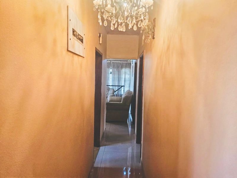 A narrow residential hallway featuring tiled flooring and a decorative chandelier, providing access to adjacent rooms.