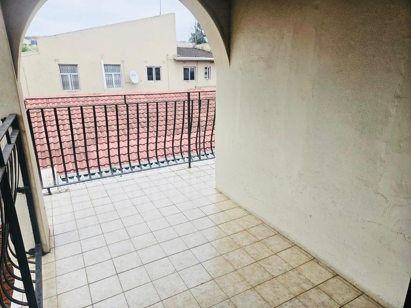 A covered balcony featuring tiled flooring, a metal balustrade, and an arched architectural detail, offering an outdoor space ready for refurbishment.