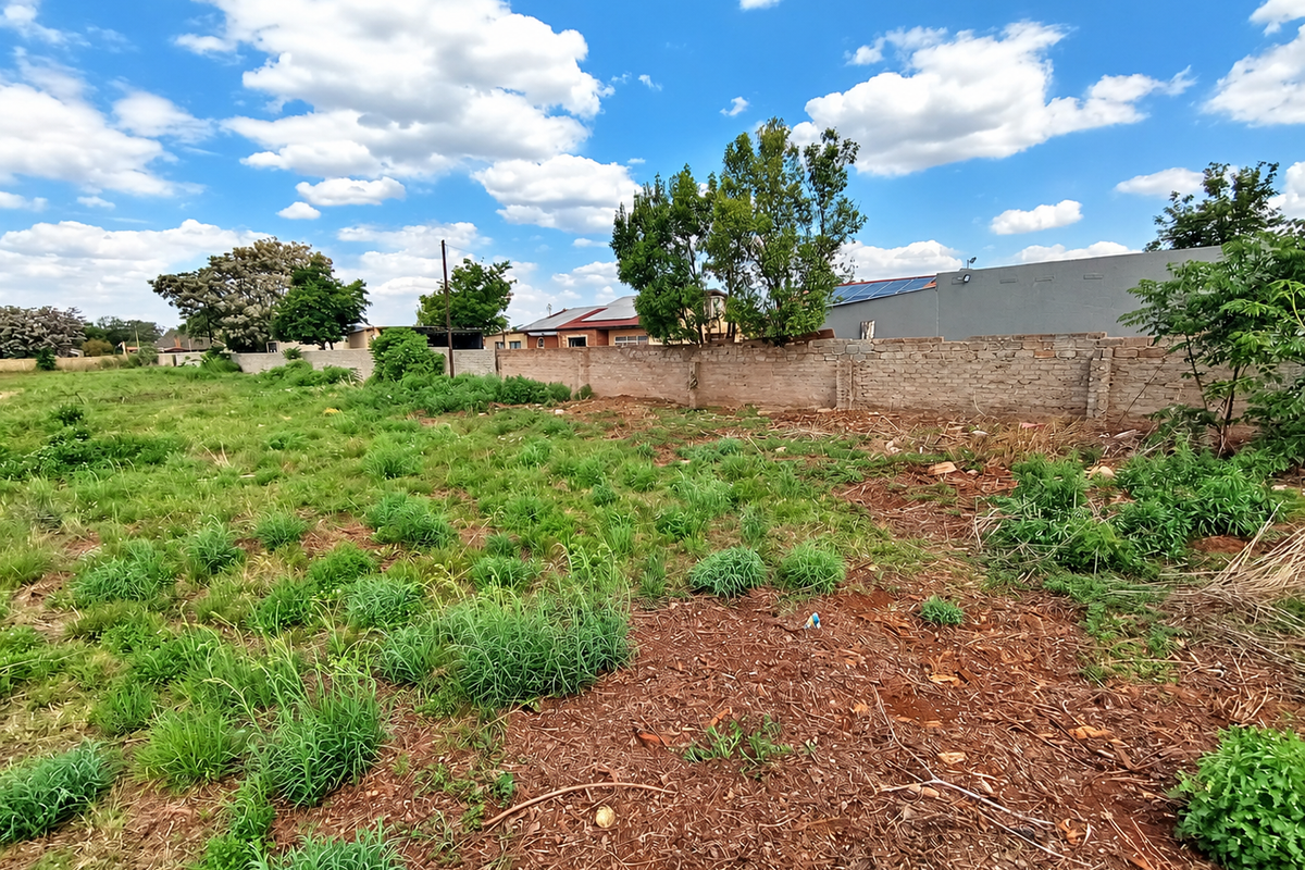 A view of a vacant residential plot featuring natural vegetation and a perimeter brick boundary wall.