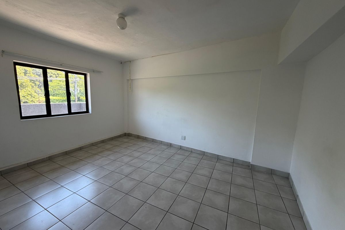An empty bedroom featuring neutral tiled flooring, white walls, and an aluminium-framed window providing natural light.