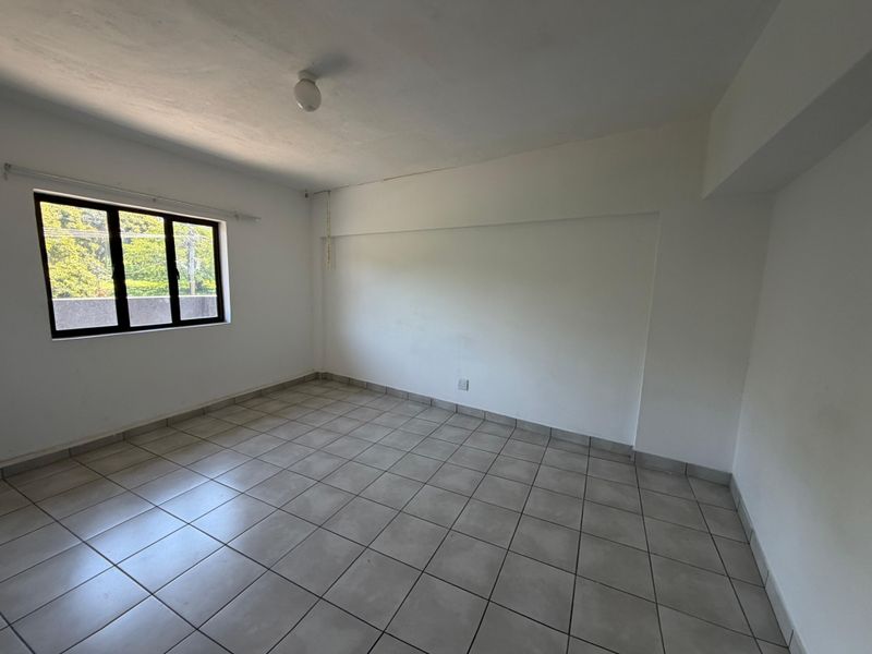 An empty bedroom featuring neutral tiled flooring, white walls, and an aluminium-framed window providing natural light.