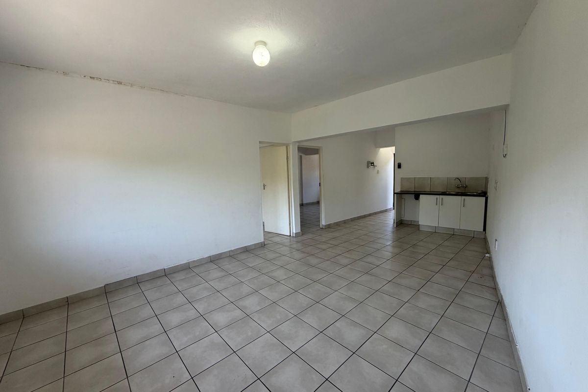An empty open-plan living and kitchen area featuring tiled flooring, basic cabinetry, and a sink, offering a blank canvas for renovation.