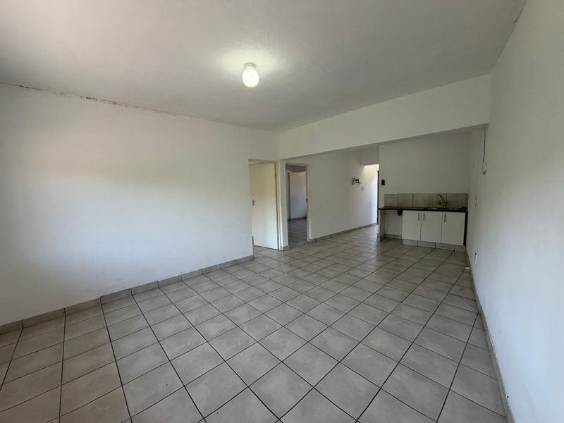 An empty open-plan living and kitchen area featuring tiled flooring, basic cabinetry, and a sink, offering a blank canvas for renovation.