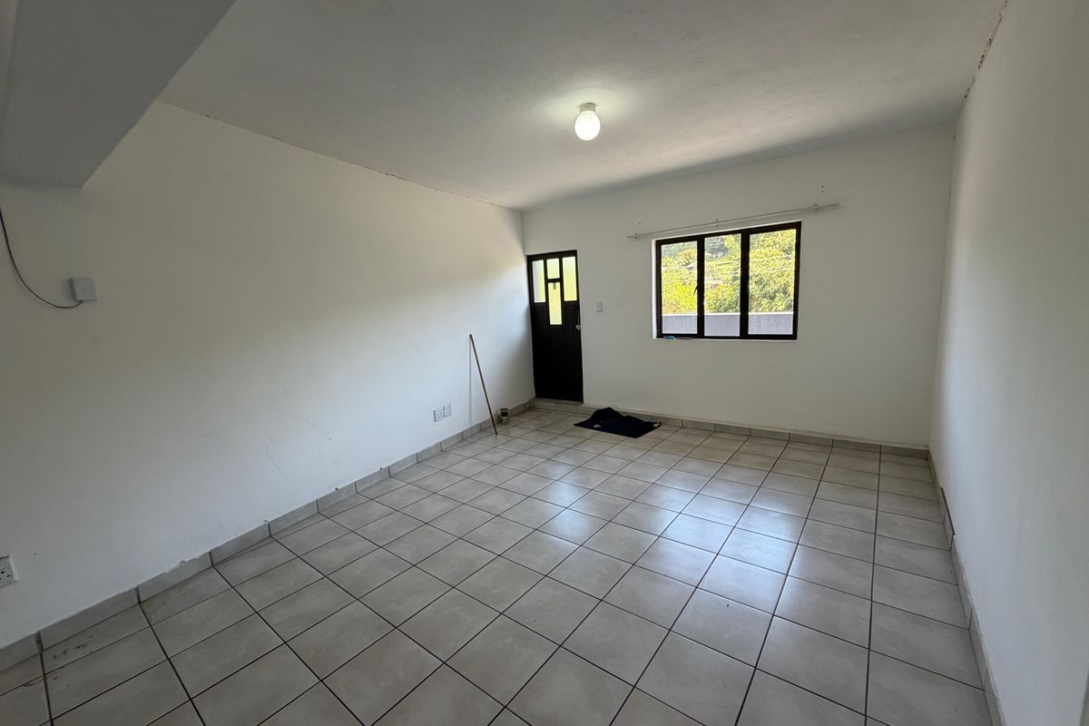 An empty, neutrally painted living area featuring tiled flooring, a window, and an external door, offering a blank canvas for personalization.