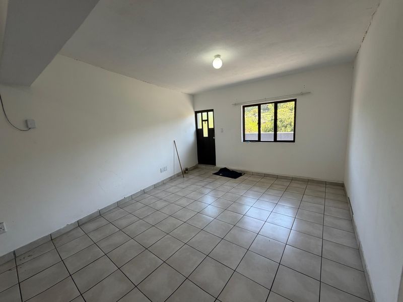 An empty, neutrally painted living area featuring tiled flooring, a window, and an external door, offering a blank canvas for personalization.
