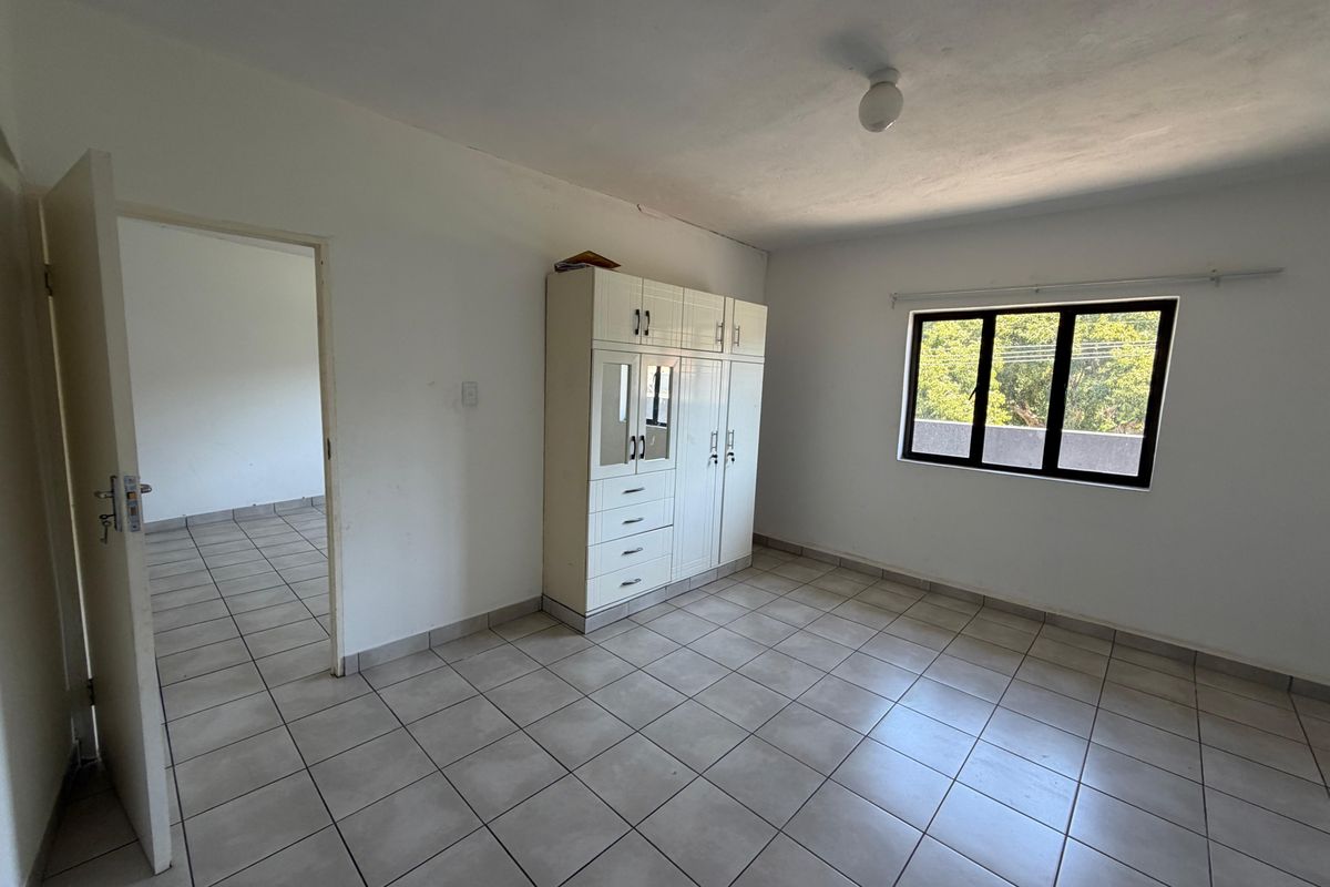 A functional bedroom featuring neutral tiled flooring, a built-in wardrobe, and a window providing natural light.