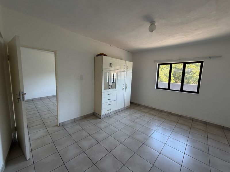 A functional bedroom featuring neutral tiled flooring, a built-in wardrobe, and a window providing natural light.