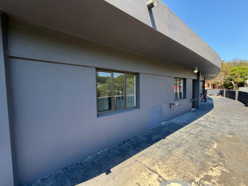 A spacious outdoor balcony area featuring a dark grey exterior finish, aluminium window frames, and a wall-mounted drying rack.