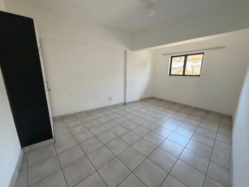 A bright, empty bedroom featuring neutral tiled flooring and a built-in cupboard, offering a clean canvas for personalization.