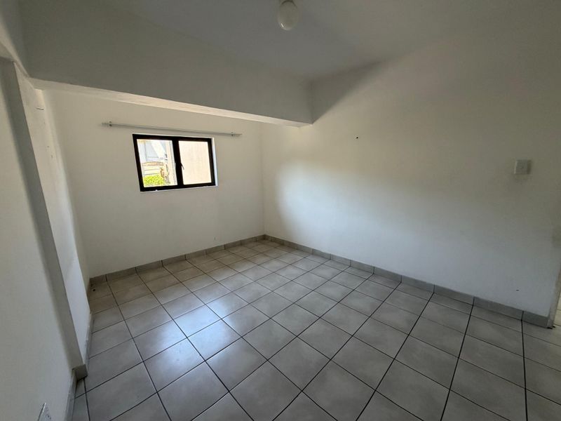 A clean, empty bedroom featuring neutral tiled flooring, a single window with a curtain rod, and a simple ceiling light fixture.