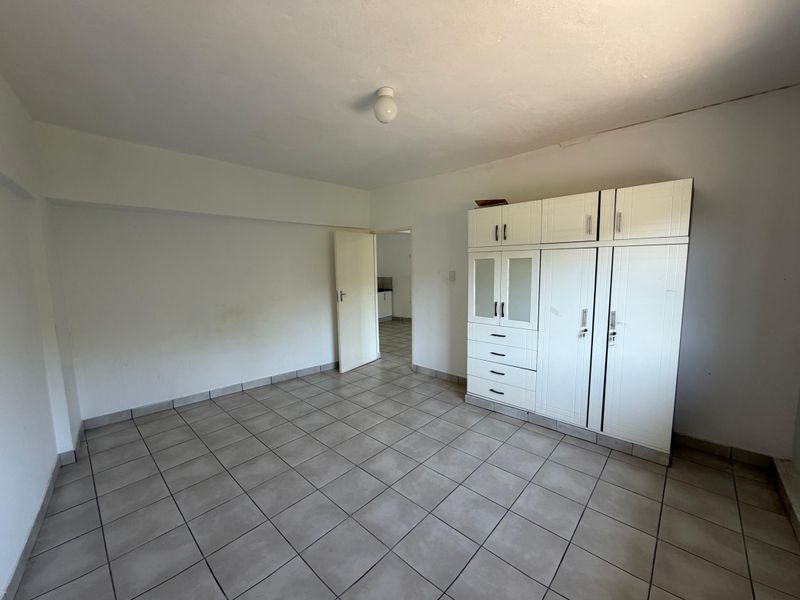 A spacious, empty bedroom featuring neutral tiled flooring and a large built-in wardrobe, offering a blank canvas for personalization.
