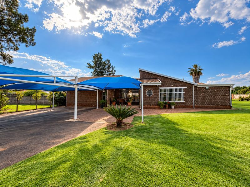 Front exterior view of a brick house featuring a large paved driveway with a blue shade cloth carport and well-maintained lawn.