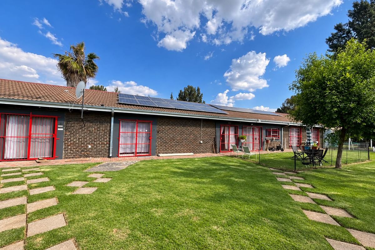 Rear view of a brick house featuring multiple sliding glass doors with security gates, a tiled roof, and installed solar panels overlooking a lawn.