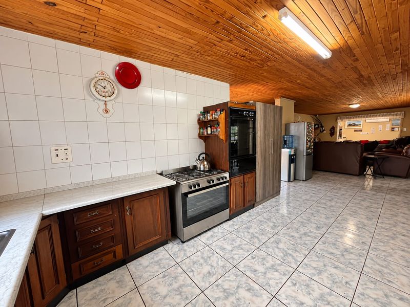 Open plan kitchen featuring timber cabinetry, gas hob, built-in oven, and a distinctive timber tongue and groove ceiling, flowing into the living area.