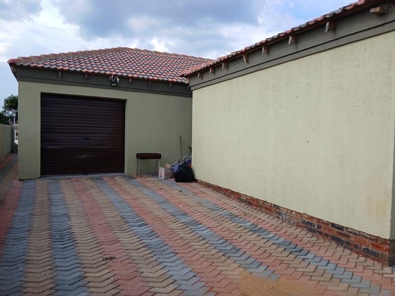 Exterior view of a single garage with a roll-up door and paved driveway, featuring plastered walls and a tiled roof.