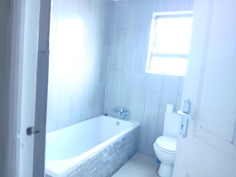 A functional bathroom featuring a bathtub with a mixer tap, a toilet, and tiled wall finishes.
